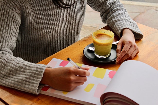 Picture of a person sitting with a coffee and writing down something