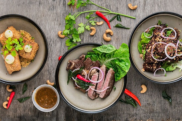 Picture of 3 different dishes on a wooden table that have meat 