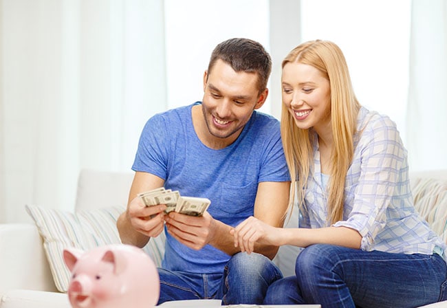 Couple sitting on a couch counting money with a piggy bank on the coffee table - habits of frugal people starts with knowing where money goes