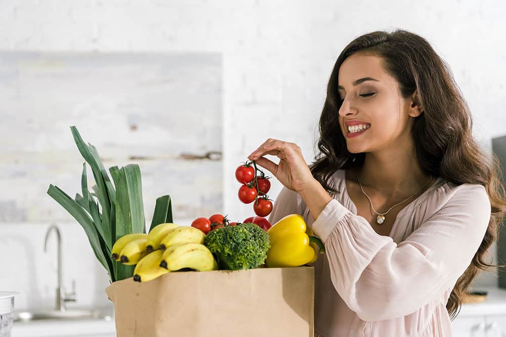 Woman putting tomatoes in a grocery bag full of fruit and vegetables